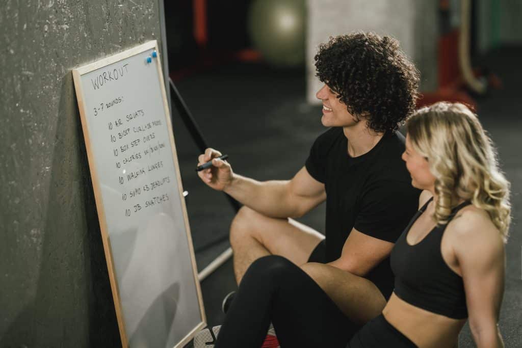 Deux personnes lisant une liste d'exercices sur tableau.