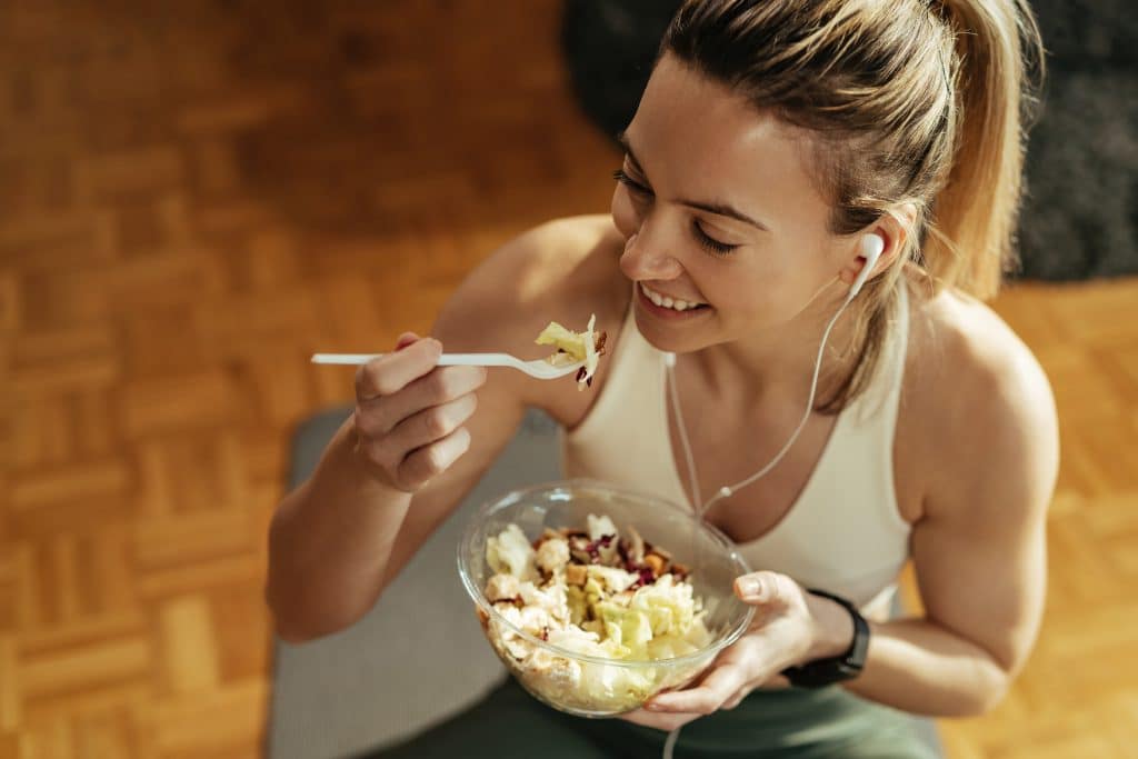 Femme mangeant une salade avec écouteurs.