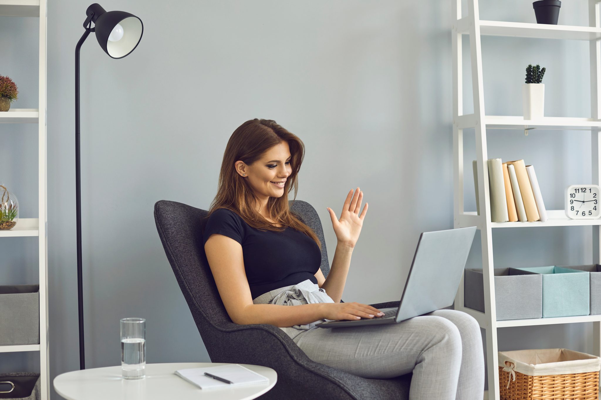 woman waving hand has video call laptop computer online sitting in armchair at home. Femme souriante en visioconférence sur ordinateur portable